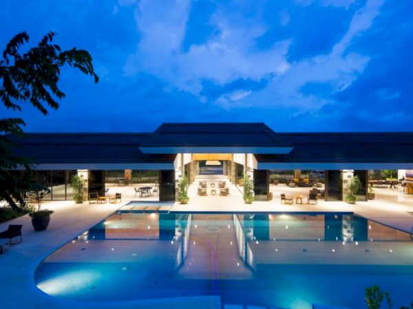 A modern building with large windows overlooks a lit swimming pool area at dusk, creating a serene and inviting atmosphere.