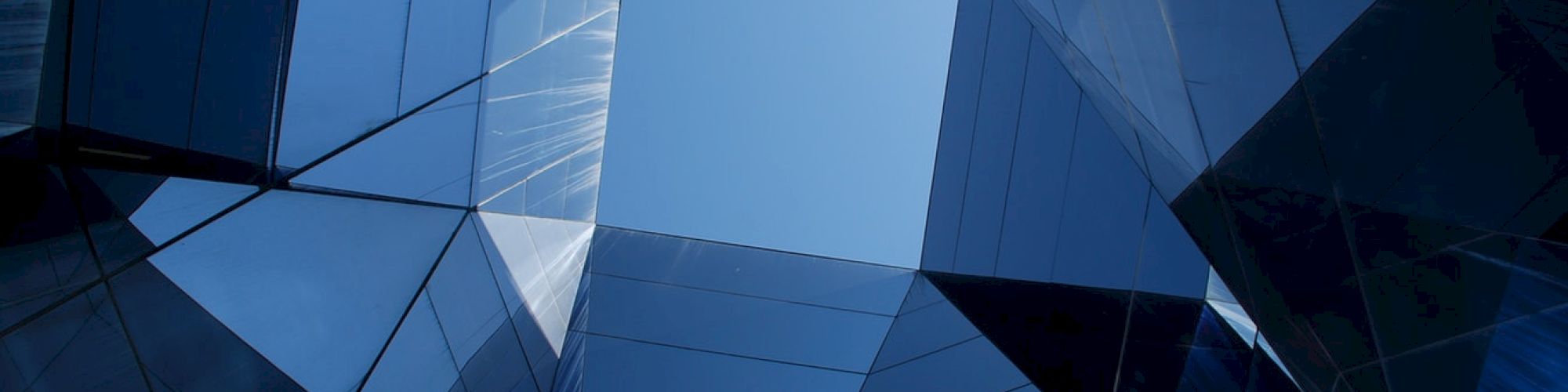 The image shows a geometric view of a building's reflective glass facade, forming a symmetrical pattern with the sky visible at the center.
