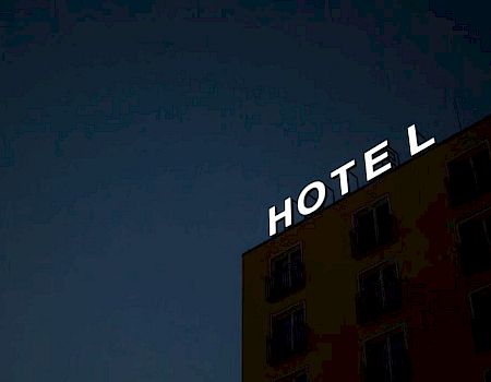 The image shows a building at night with an illuminated "HOTEL" sign on the roof against a dark sky.