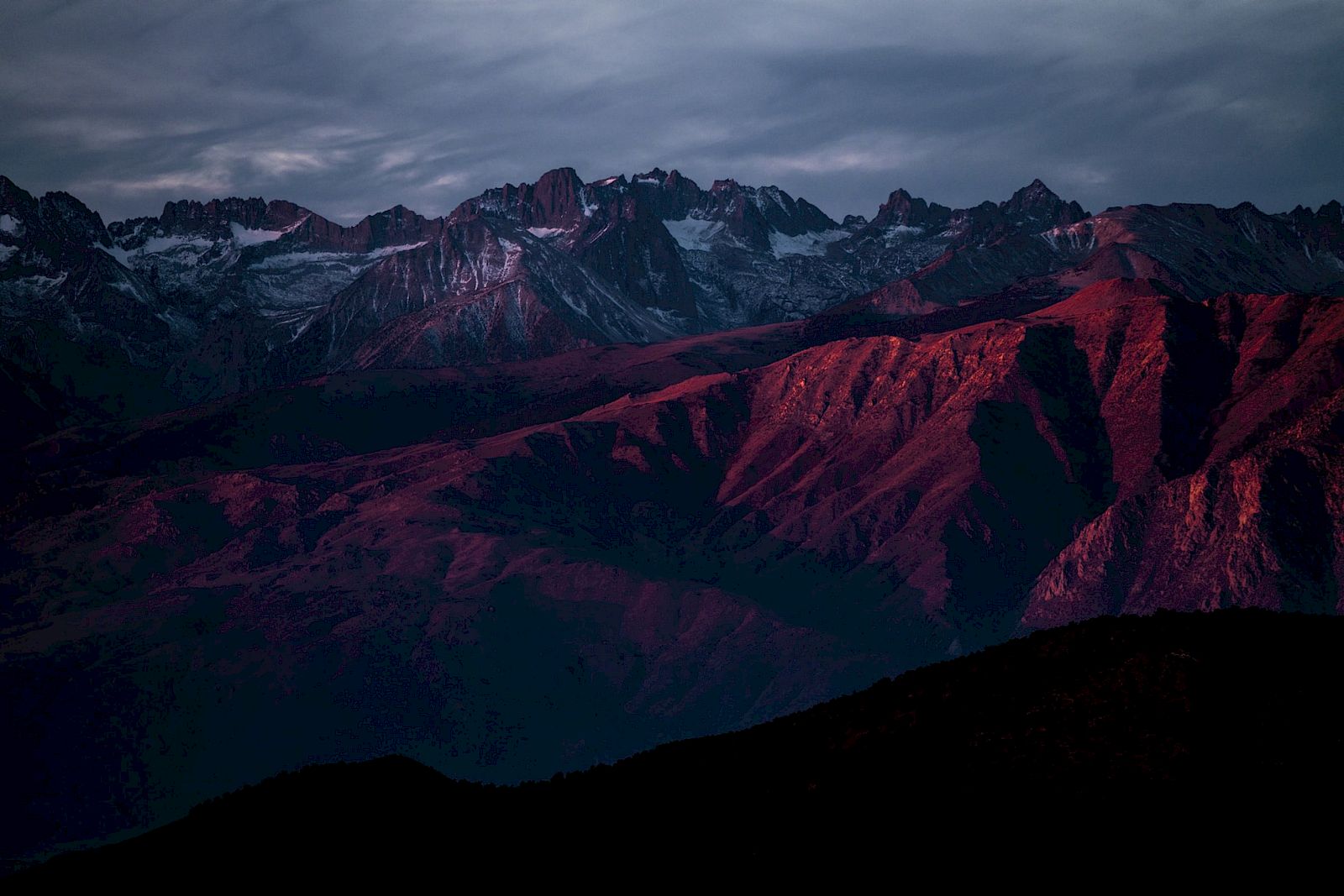 A mountain range is bathed in red and purple hues under a dramatic sky, creating a striking contrast in the landscape.