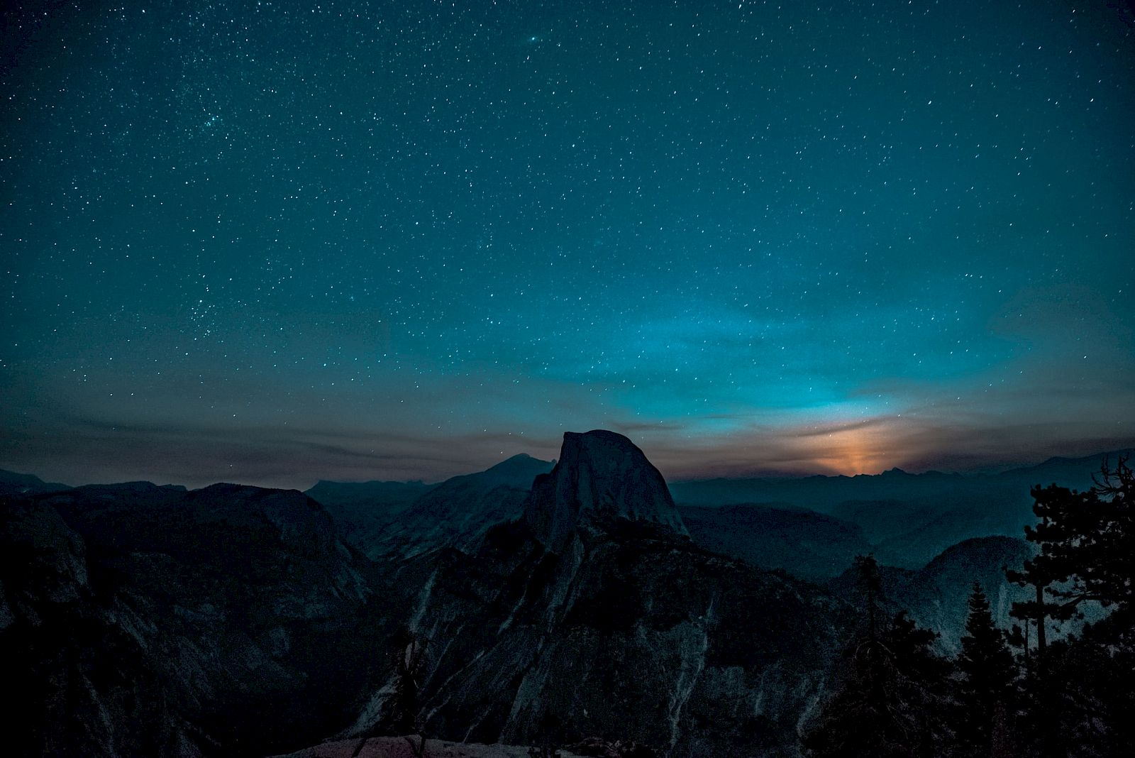 A serene nighttime landscape with a mountainous silhouette under a starry sky and a glow from the horizon.