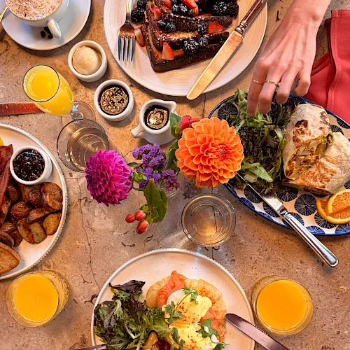 Brunch spread with stacked French toast/waffles, sunny eggs, salad and pastries, juice and coffee, plus fresh flowers on the table.