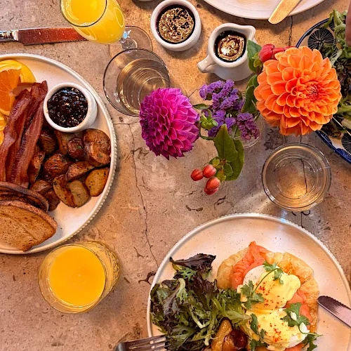 A brunch spread with breakfast plates, bacon and potatoes, salad, poached eggs, and orange juice plus coffee and condiments.