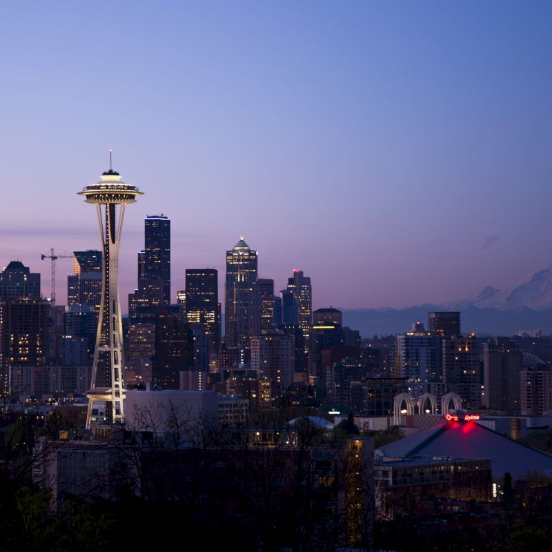 The image shows a city skyline at dusk with a prominent tower and a mountain in the background.