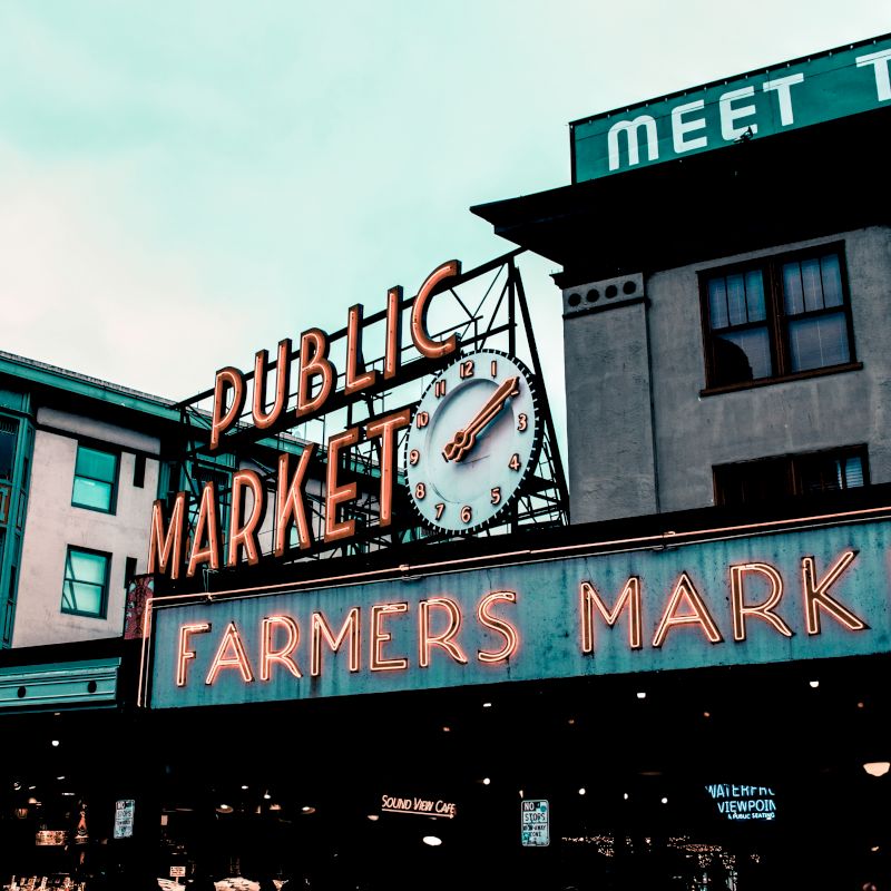 The image shows a public market sign with a clock, known for being a lively farmers market in an urban setting.