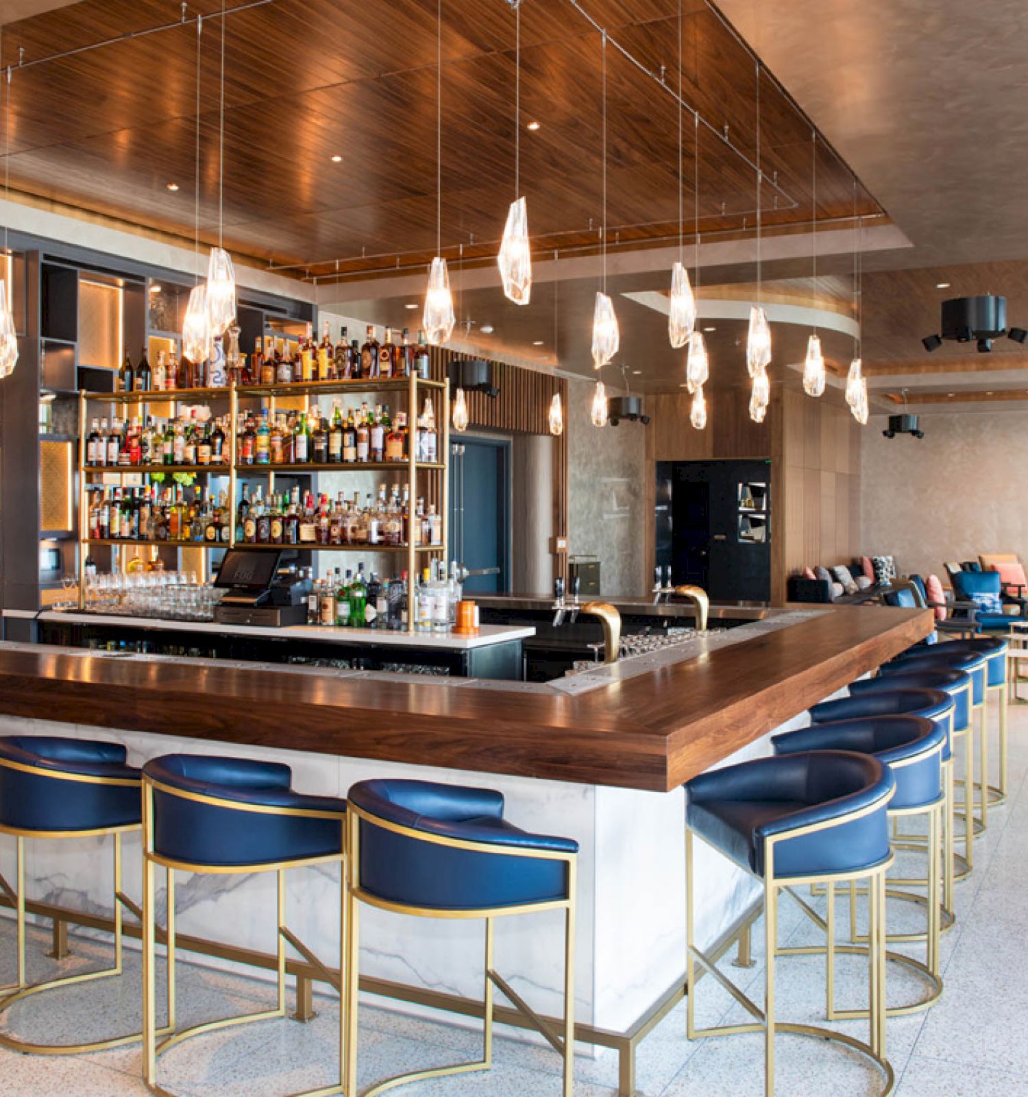 The image shows a stylish bar with bar stools, a well-stocked counter, and modern lighting in a spacious interior.