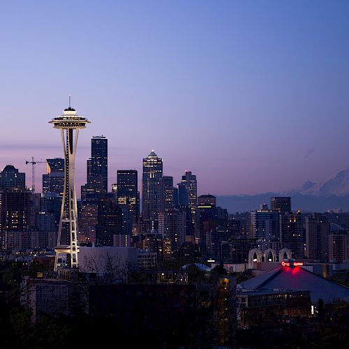 The image shows the Seattle skyline at dusk with the illuminated Space Needle and Mount Rainier visible in the background.