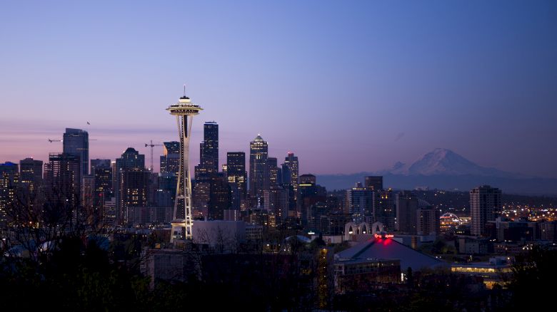 Seattle skyline at dusk, featuring the Space Needle and Mount Rainier in the background, under a soft, dimming sky.