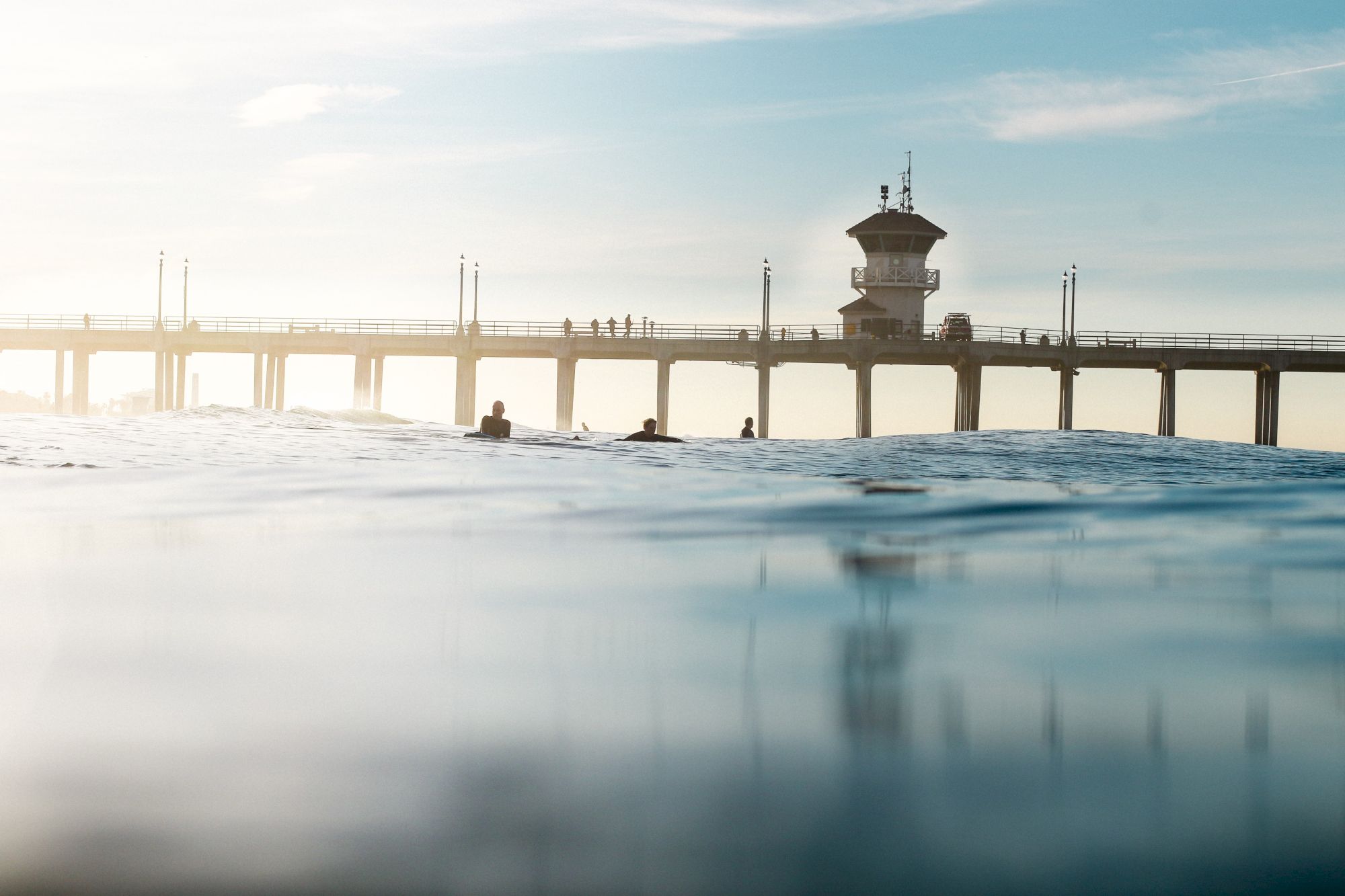 A pier extends over the ocean with a tower structure, seen from water level under a clear sky.